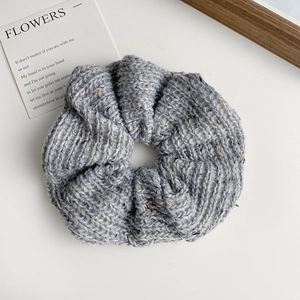 Close-up of grey knitted oversized scrunchie with colorful flecks on white surface