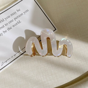 Close-up of pearl white wavy acetate hair claw clip with golden metal teeth