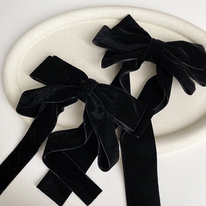 Detailed view of two black velvet bow hair clips with long ribbons on a textured tray