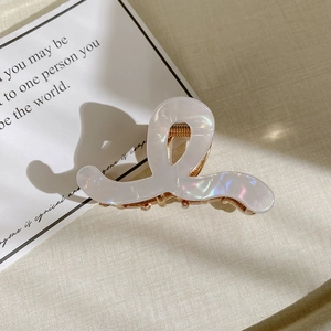 Detail view of pearl white acetate hair claw clip with golden metal base on beige fabric