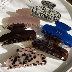 Detailed close-up of six assorted acetate hair claws with elegant gold logo detailing