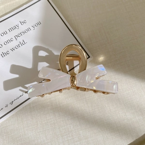 Macro shot of bow-shaped hair claw clip with golden metal and iridescent pearlescent inlay