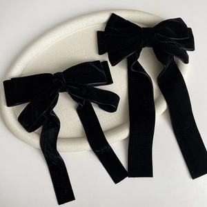 Elegant black velvet bow hair clips in two sizes on a white minimalist display tray