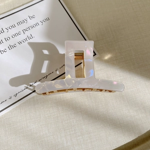 Detail view of pearlescent white acetate hair claw with golden spring on textured background