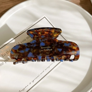 Detail of tortoiseshell acetate hair claw clip with golden logo on white tray