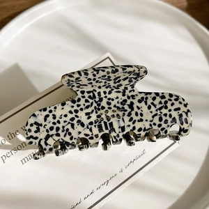 Detail view of acetate claw clip with marble pattern and gold logo in French retro style