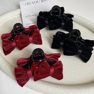 Close-up of velvet bow hair claws in burgundy and black on an elegant woven tray
