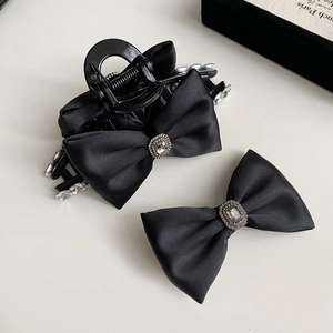 Close-up of black satin bow hair clip with central rhinestone detail on white background