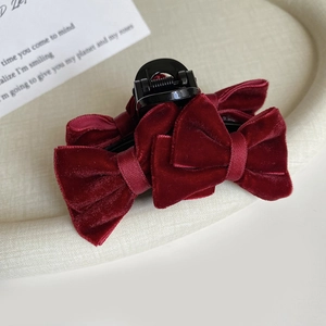 Detail of elegant wine red velvet bow hair claw clip on a decorative beige display tray