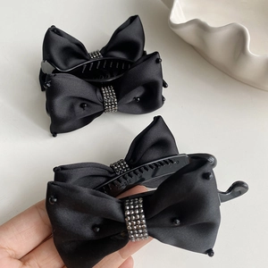 Detailed view of black satin bow hair clip featuring a sparkling rhinestone center band