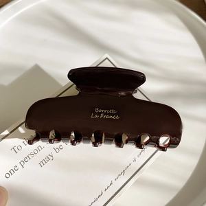 Macro detail of glossy dark acetate hair claw clip with Borrettc La France golden lettering