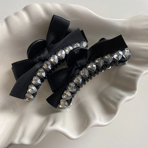 Close-up of black ribbon bow hair clips with heart-shaped rhinestones in a white tray