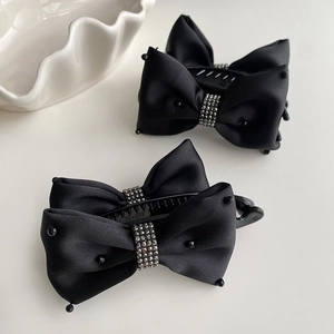 Close-up of black satin bow hair clips with sparkling rhinestone centers and bead details
