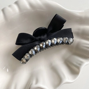 Close-up of black satin ribbon hair claw with sparkling heart-shaped rhinestones on a tray