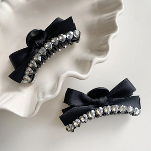 Elegant black ribbon bow hair claw clips with heart rhinestones on a white plate