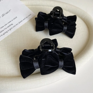 Detailed view of two elegant black velvet bow hair claws on a textured beige tray
