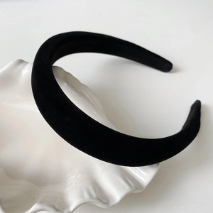 Détail du serre-tête en velours noir épais posé sur un plateau décoratif blanc ondulé