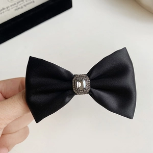 Detail of elegant black satin bow hair clip featuring a large central crystal and rhinestones