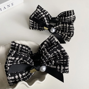 Detail of tweed bow hair clip with black ribbon, white pearl, and gold metal accents