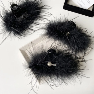 Close-up of black feather hair clips with rhinestones and ribbon detail on white surface