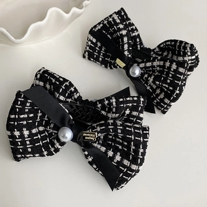 Detail of tweed bow hair clip with white pearl and golden brand tag on grey background