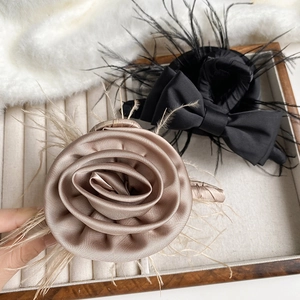 Close-up of champagne satin rose and black bow hair claw clips with feather accents