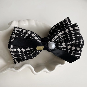 Close-up of black and white tweed bow hair clip with faux pearl and gold metal detail