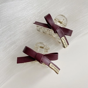 Dettaglio di pinze per capelli con fiocco in pelle bordeaux e targhette metalliche oro