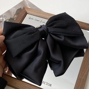 Détail de la pince à cheveux noeud en satin noir avec strass et emblème en métal