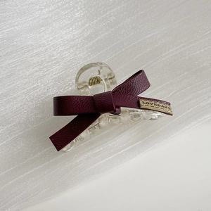 Dettaglio molletta per capelli con fiocco in pelle bordeaux e logo dorato su raso