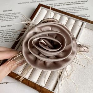 Detailed close-up of champagne brown rose hair claw with elegant feathers and satin petals