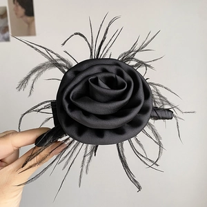 Elegant black satin rose hair clip with feathers in a vintage style held by hand