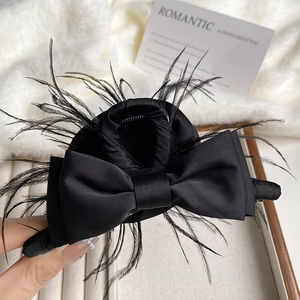Detailed close-up of a black satin bow hair claw with elegant feather accents for women