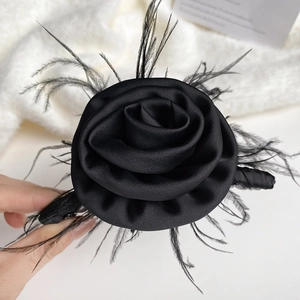 Detail of elegant black satin rose hair clip with delicate feather accents on white fur