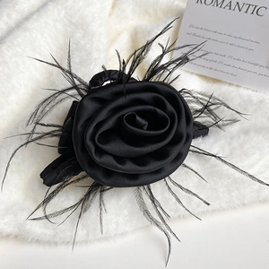 Detailed close-up of a black satin rose and soft feather hair claw on a white fur surface