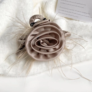 Elegant champagne silk rose hair claw clip with feather accents on white plush background