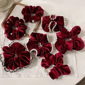 Set of dark red velvet scrunchies with pearls and lace edges on a white background