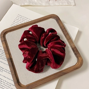 Elegant deep red velvet scrunchie with white pearls on a minimalist wood tray display