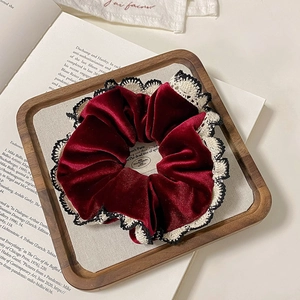 Velvet hair scrunchie in deep red with lace trim on a rustic wooden tray background