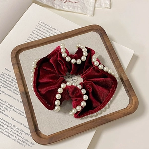 Close-up of velvet scrunchie in burgundy with pearl beads on a wooden display tray
