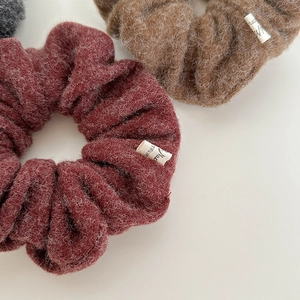 Detailed close-up of burgundy and brown plush fabric scrunchies with white labels