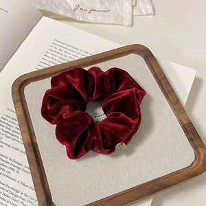 Detailed shot of dark red velvet scrunchie with golden charm on a wooden tray