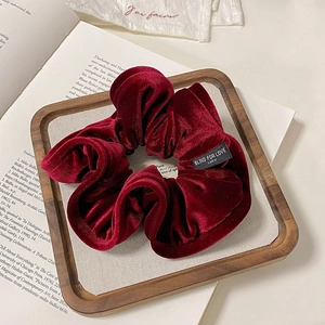 Close-up of velvet scrunchie in burgundy red on wooden tray with vintage book background