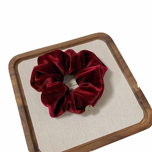 Luxurious burgundy velvet oversized scrunchie with a gold metal charm on a wooden tray