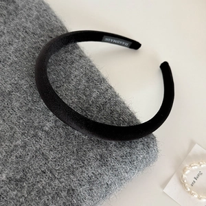 Close-up of a handmade black velvet headband with label on a grey knitted texture