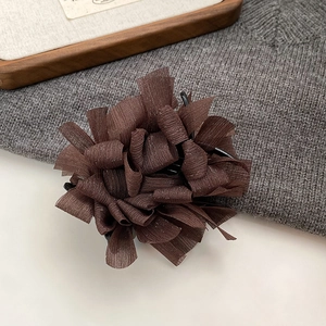 Dettaglio del fermaglio per capelli in chiffon plissettato color caffè su fondo in maglia