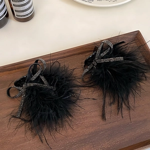 Close-up of black feather hair clips with sparkling rhinestone bow details on wooden tray