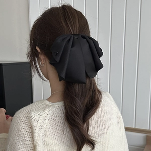 Close-up of a large black satin bow hair claw clip worn on a low ponytail for women