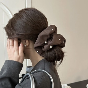 Détail d'un chouchou en tissu marron avec perles blanches sur une coiffure queue de cheval