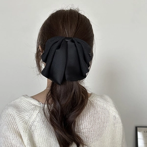 Detail view of a large black satin bow hair claw clip styled on a low ponytail hairstyle